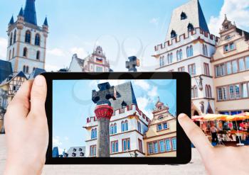 travel concept - tourist takes picture of medieval Market cross with medieval permission for town to have a market in Trier, Germany on smartphone,