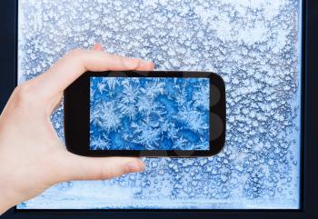 travel concept - tourist takes picture of snowflakes and frost pattern on window in cold winter evening on smartphone,