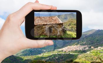 travel concept - tourist takes picture of mountain landscape with Savoca village in Sicily in spring on smartphone, Italy