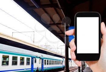 travel concept - tourist photograph railway platform and train in Italy on smartphone with cut out screen with blank place for advertising logo