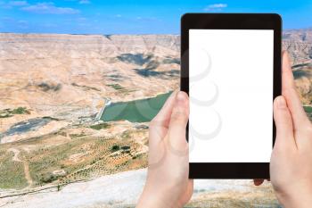 travel concept - tourist photograph valley of Wadi Al Mujib river and dam, Jordan on tablet pc with cut out screen with blank place for advertising logo