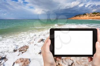 travel concept - tourist photograph crystal salt beach on Dead Sea coast, Jordan on tablet pc with cut out screen with blank place for advertising logo