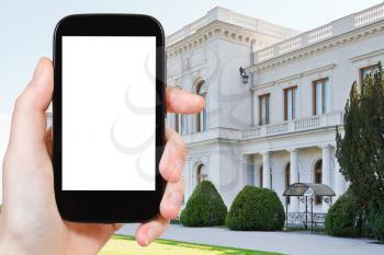 travel concept - tourist photograph white Grand Livadia Palace in Crimea on smartphone with cut out screen with blank place for advertising logo
