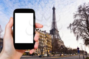 travel concept - tourist photograph eiffel tower from quai branly in Paris on sunset on smartphone with cut out screen with blank place for advertising logo