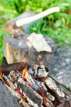 firewood burning in rusty brazier close up with ax in stump on background