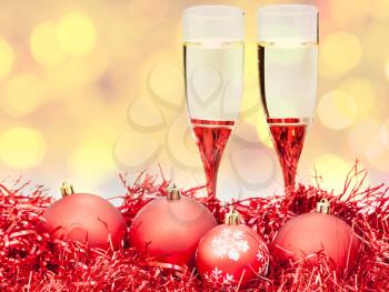 Christmas still life - two glasses of champagne at red Xmas decorations with yellow and violet blurred Christmas lights background