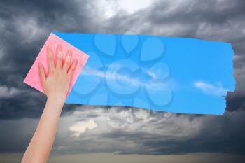 weather concept - hand deletes storm clouds by pink cloth from image and blue sky with white clouds are appearing
