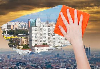 ecology concept - hand deletes smog in city by orange cloth from image and clear houses are appearing