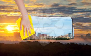 weather concept - hand deletes yellow sunrise over city by yellow cloth from image and day cityscape is appearing