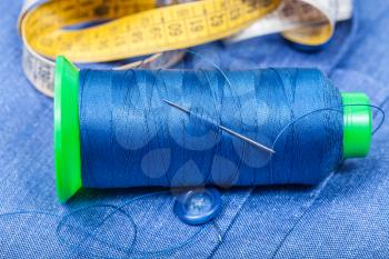 tailoring still life - thread bobbin with needle, button, measure tape on blue silk cloth