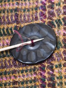 attaching of button to woolen fabric by needle close up
