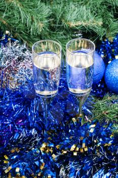Christmas still life - Two glasses of champagne with blue Xmas baubles and tinsel and on Christmas tree background