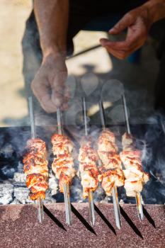 man cooks pork shish kebabs on outdoor brazier