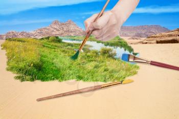 nature concept - seasons and weather changing: hand with paintbrush paints green meadow in sand desert