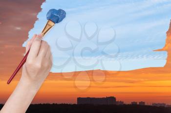 nature concept - seasons and weather changing: hand with paintbrush paints blue daily sky on orange sunset sky