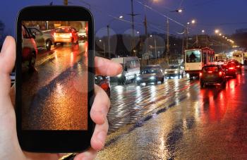 travel concept - tourist photographs picture of night car traffic on streen in rain on smartphone