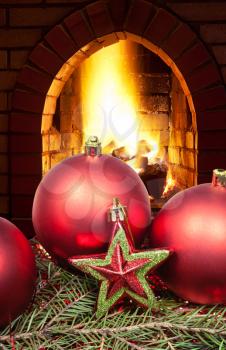 red star and Christmas balls on green spruce tree with open fire in home fireplace