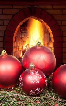 red Christmas balls on green spruce tree with open fire in home fireplace
