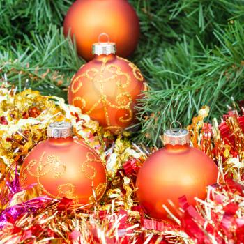 Christmas still life - several orange and yellow Christmas baubles, red tinsel on green Xmas tree background