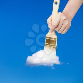 weather concept - hand with paintbrush paints white little cloud in the summer blue sky