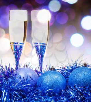 Christmas still life - two glasses of sparkling wine at blue Xmas decorations with violet blurred Christmas lights bokeh background
