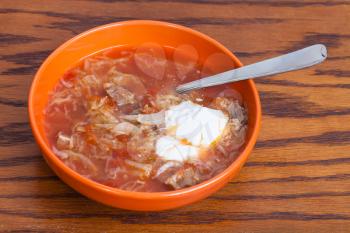 cabbage soup in meat broth with sour cream in ceramic bowl with tablespoon on wooden table