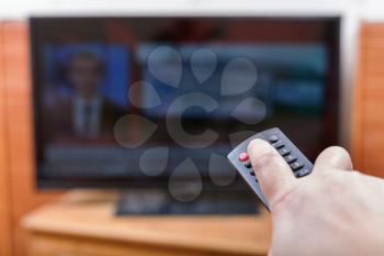 Hand turns off News on TV channel by remote control in living room