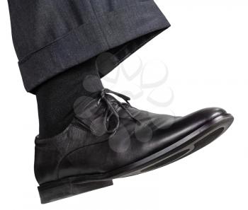 side view of male right foot in black shoe takes step isolated on white background