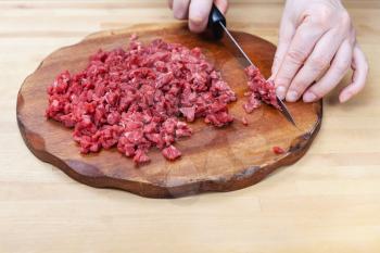 woman finely chops meat on wooden cutting board on table