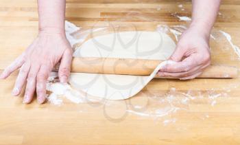 front view of female hands roll out the dough with a rolling pin on wooden table
