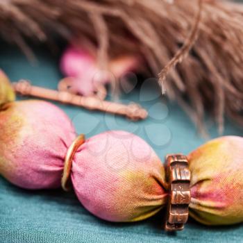 textile necklace from pink and yellow painted silk balls and copper rings close up on green background