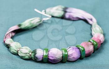 textile necklace from violet and green painted silk balls and green ceramic rings on green background