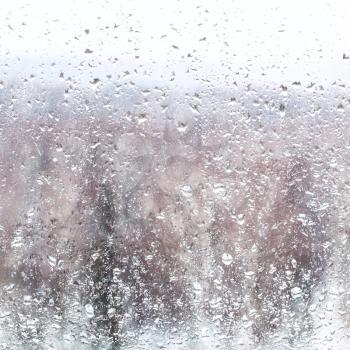 water drops from melting snow during snowfall on home window in winter