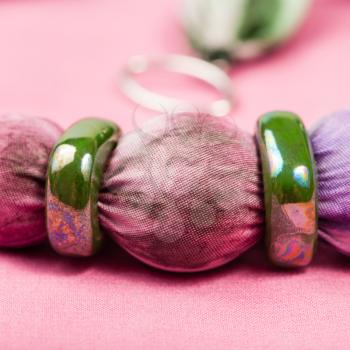 detail of handmade textile necklace - violet painted silk batik bead and green ceramic rings close up on pink background