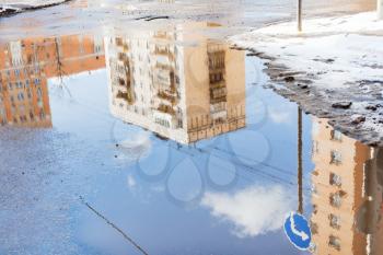 urban houses and sky with clouds reflected in puddle from melting snow on street in sunny spring day