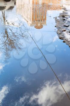 puddle from melting snow on street with reflection of urban house in sunny spring day