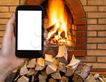 comfortable holiday concept - tourist photographs fireplace on smartphone with cut out screen with blank place for advertising