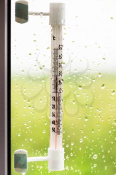 thermometer and rain drops on window glass in summer day