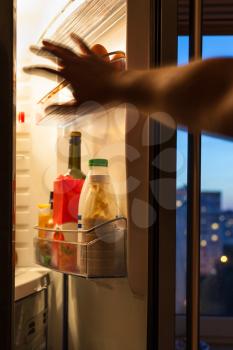 hand goes for food in refrigerator at home in evening