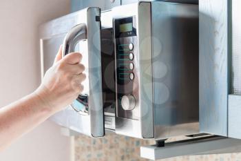 hand opens door of microwave oven for heating food