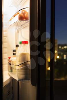 Open door of refrigerator with milk bottles in night