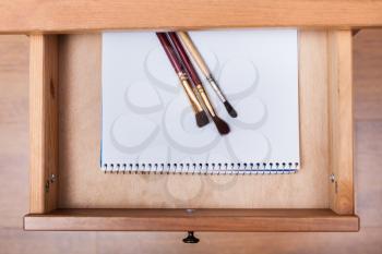 above view of paint brushes on drawing album in open drawer of nightstand