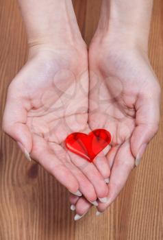 one red heart in female hands with wooden background