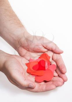glass heart above pile of paper hearts on male palms on white background