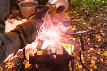 Welder welds iron ring in outdoor rural workshop