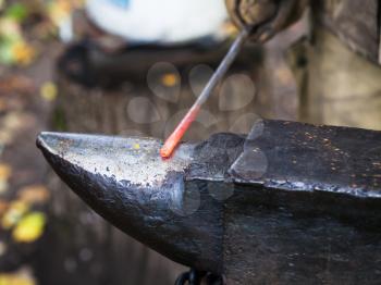 red hot iron rod on anvil in outdoor rural smithy