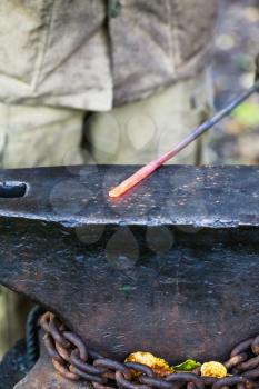 red hot glowing steel rod on anvil in outdoor rural smithy