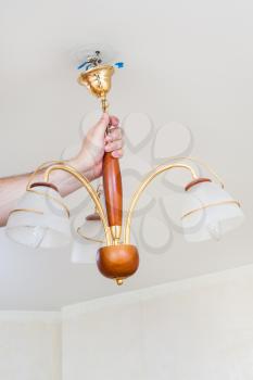 electrician removes hanging ceiling chandelier for repairing in room