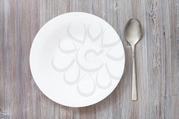top view of one white deep plate and spoon on gray brown table