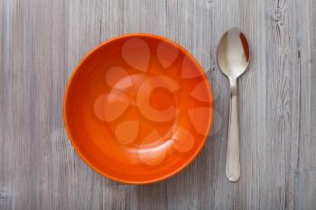 top view of one orange bowl and spoon on gray brown table
